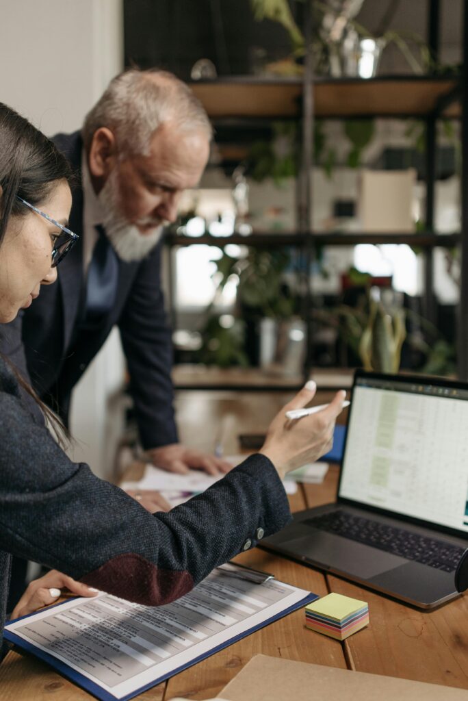 pexels-photo-7654496-7654496 A business professional explains data to a colleague using a laptop and documents in an office setting.